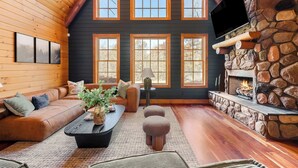 A cozy living room with a stone fireplace, wooden walls, and large windows. - Shenandoah Mansion (Elkton)