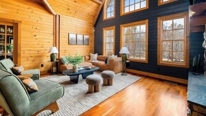 A cozy cabin interior with wooden walls, a high ceiling, and large windows offering a view of the outdoors. - Shenandoah Mansion (Elkton)