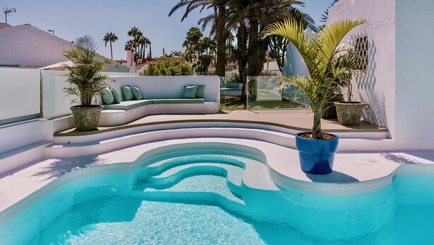 A pool with a curved edge, surrounded by white walls and green plants.
