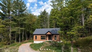 Une maison de plain-pied avec un toit en pente, entourée d’une zone boisée.