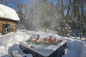 Ein Whirlpool in verschneiter Winterlandschaft, im Hintergrund eine Holzhütte.