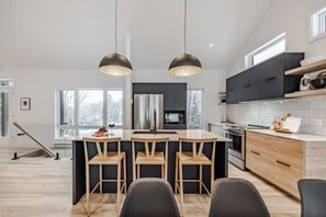 Uma cozinha moderna com ilha central, luminárias pendentes e vista para o exterior.