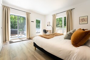 Ein modernes Schlafzimmer mit einem großen Bett, einem Schreibtisch und Blick ins Freie.