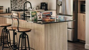 Eine moderne Küche mit Holzschränken, einer zentralen Kochinsel mit Barhocker, einem Edelstahlkühlschrank und Pendelleuchten.