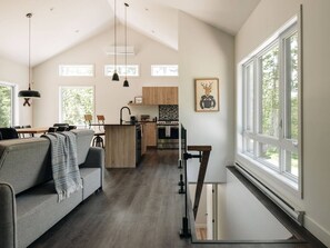 A modern kitchen with a central island, a dining area with a sofa, and large windows providing natural light.