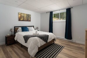 Un dormitorio con una cama grande, una mesita de noche, una lámpara, una ventana con cortinas y un cuadro en la pared.