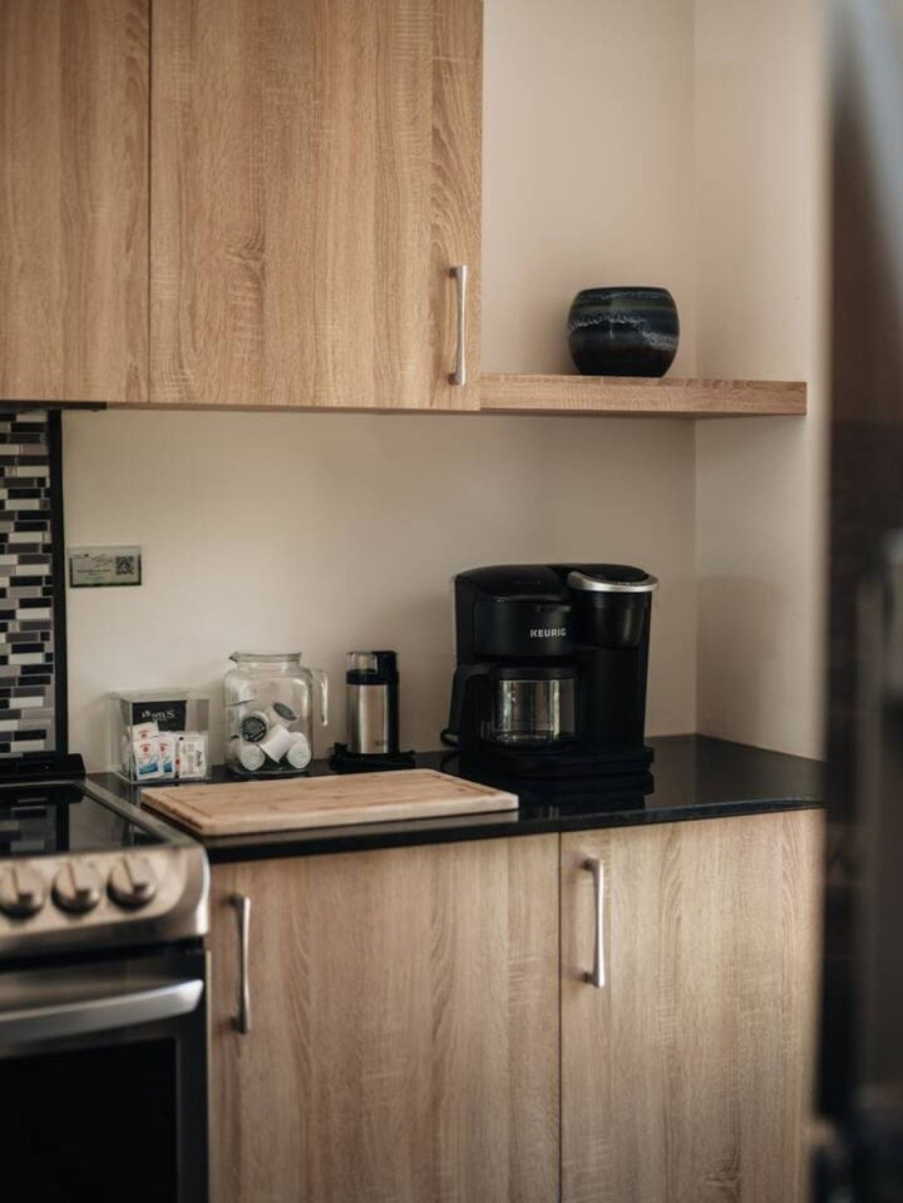 Une cuisine avec des meubles en bois, une machine à café, une planche à découper et une cuisinière.