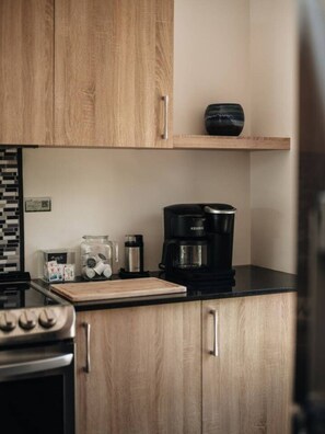 Una cocina con armarios de madera, cafetera, tabla de cortar y estufa.
