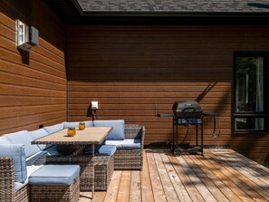 Un patio al aire libre con terraza de madera, un comedor, una parrilla y un equipo de aire acondicionado instalado en la pared.