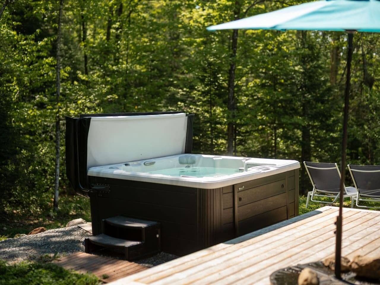 A hot tub outdoors with a wooden deck and chairs.
