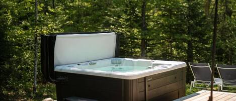 A hot tub outdoors with a wooden deck and chairs.