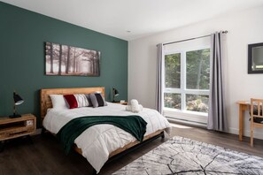 Un dormitorio con cama, mesitas de noche, una ventana con cortinas y un cuadro en la pared.