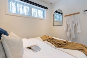 Un dormitorio con cama, ventana, espejo y una bata colgada en la pared.