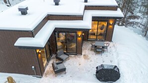 A modern building with a snow-covered roof, large glass windows, and outdoor seating area. - Private Spa| Hiking| Skiing| Mini Chalet| Assinie (Brownsburg)