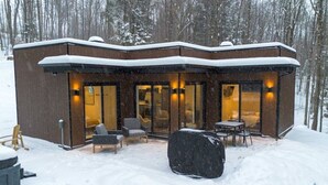 A modern building with large windows, outdoor seating, and a snow-covered roof. - Private Spa| Hiking| Skiing| Mini Chalet| Assinie (Brownsburg)