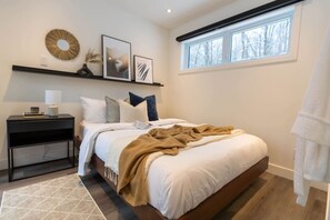 Une chambre à coucher avec un lit, une table de chevet, une lampe et une œuvre d’art accrochée au mur.