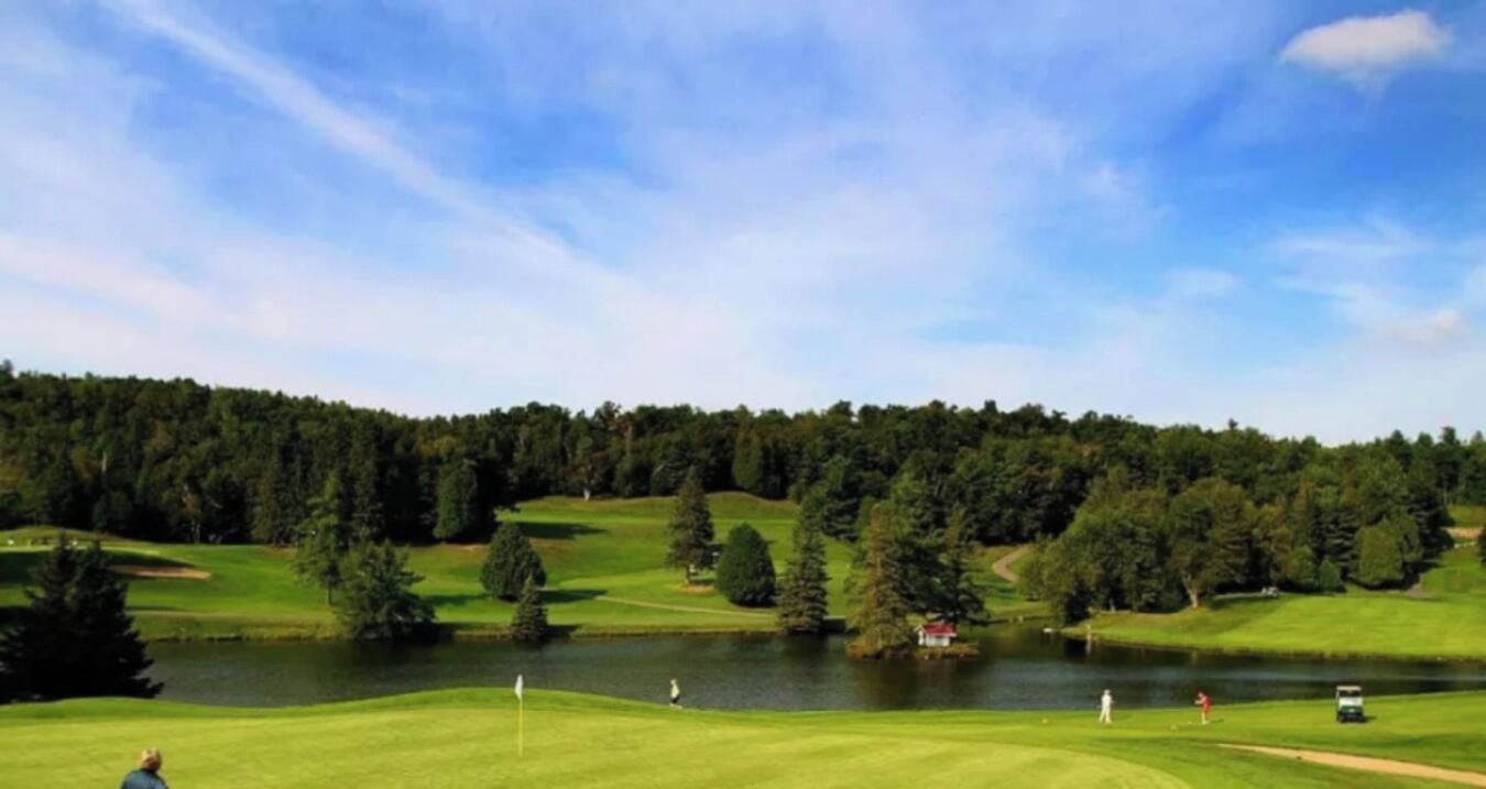 Un campo de golf con un lago, árboles y un cielo despejado.