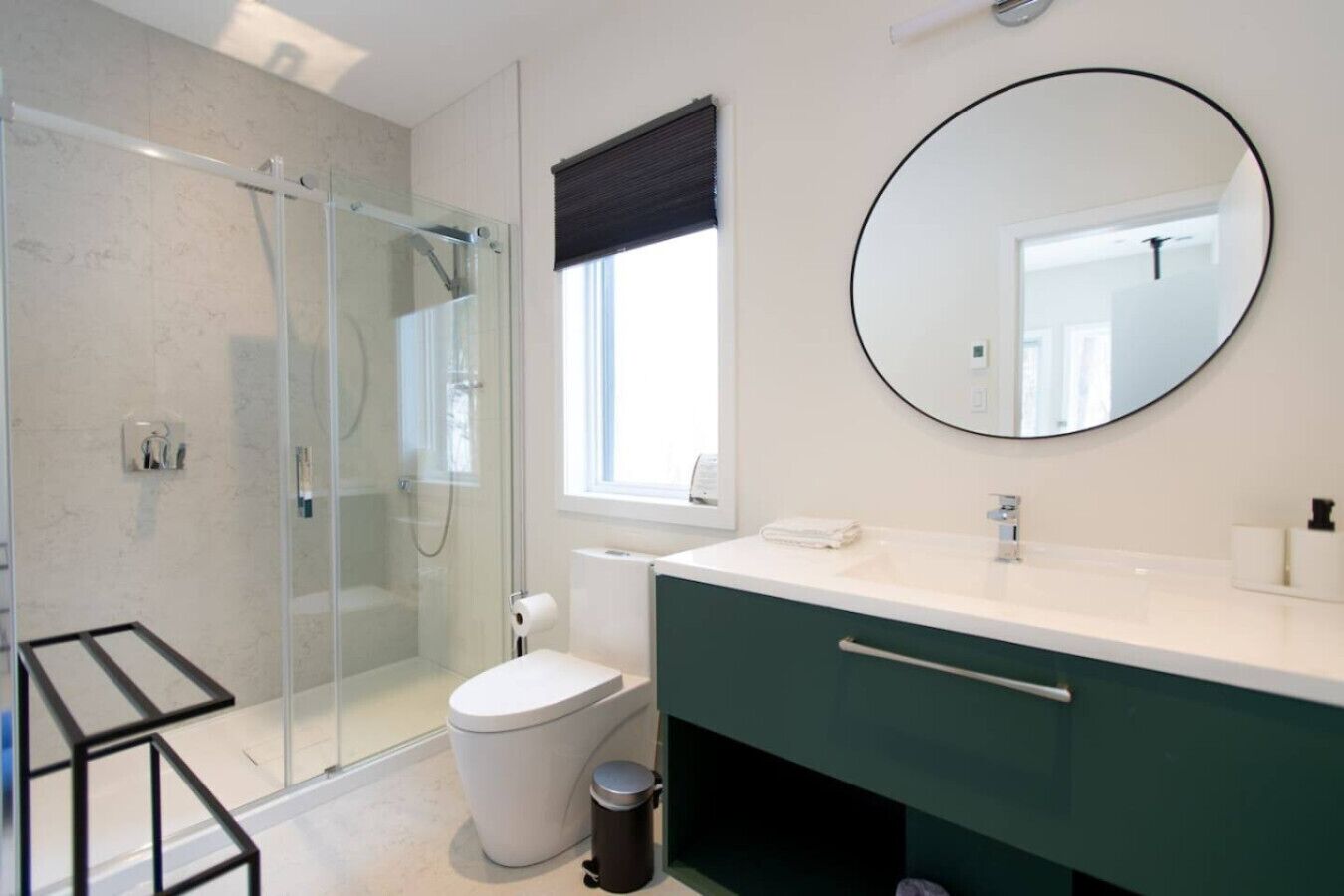 A modern bathroom with a glass shower enclosure, a toilet, a sink with a mirror, and a window.
