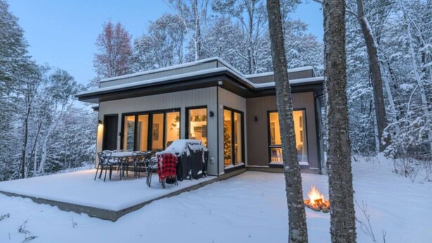 A modern house with a covered patio, large windows, and a fire burning outside. - Private Spa | Hiking | Skiing | Mini - Prime Hill (Brownsburg)