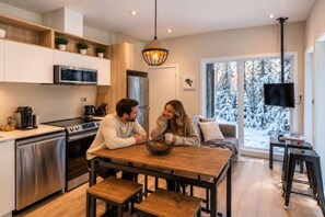 Une cuisine moderne dotée d’appareils électroménagers en acier inoxydable, d’une table à manger en bois et d’une grande fenêtre offrant une vue sur des arbres couverts de neige.
