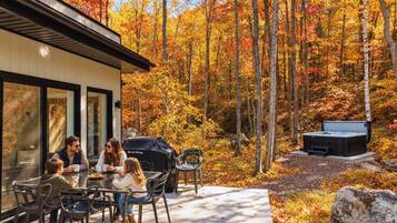 Un patio con mobiliario exterior, una parrilla y un jacuzzi en un área boscosa.