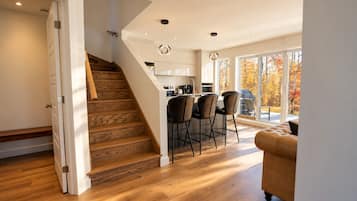 Una cocina moderna con una isla central, un comedor con sillas y una escalera que lleva a otro nivel.