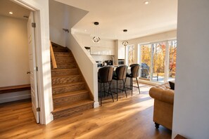 Een moderne keuken met een centraal eiland, een eethoek met stoelen, en een trap naar een hoger niveau.
