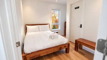 A bedroom with a wooden bed, white bedding, a bench, a window with a view of autumn trees, and a door marked 'Employees Only'.