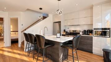 A modern kitchen with a central island, bar stools, stainless steel appliances, and a staircase leading to another level.