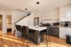 Une cuisine moderne dotée d’un îlot central, de tabourets de bar, d’appareils électroménagers en acier inoxydable et d’un escalier menant à un autre niveau.