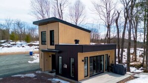A modern two-story house with a garage, large windows, and a covered outdoor seating area.