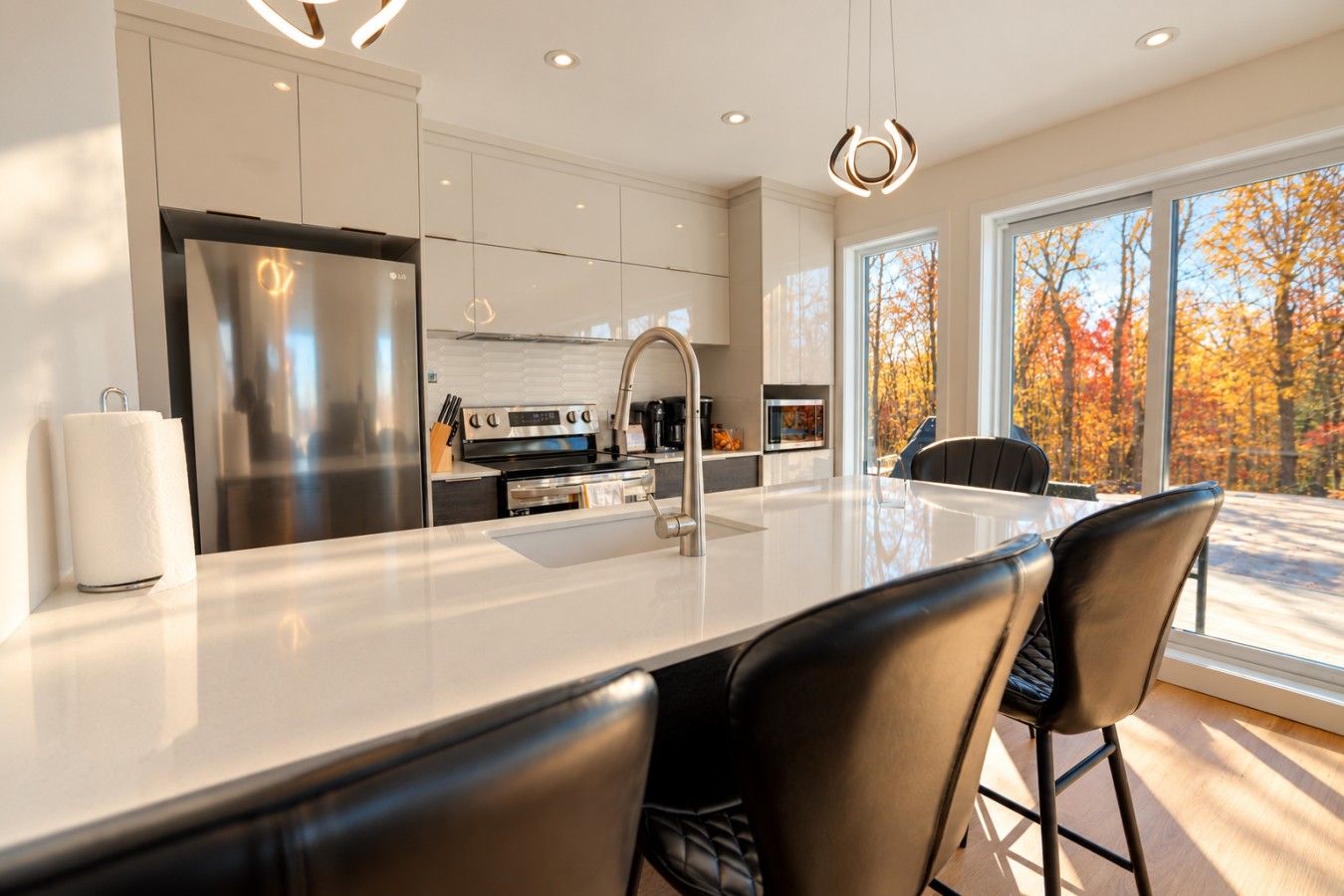 A modern kitchen with a large island, stainless steel appliances, and a view of autumn trees.