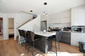 A modern kitchen with a central island, bar stools, and a dining area.