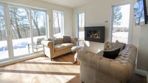 A spacious living room with a fireplace, large windows, and a view of the outdoors.