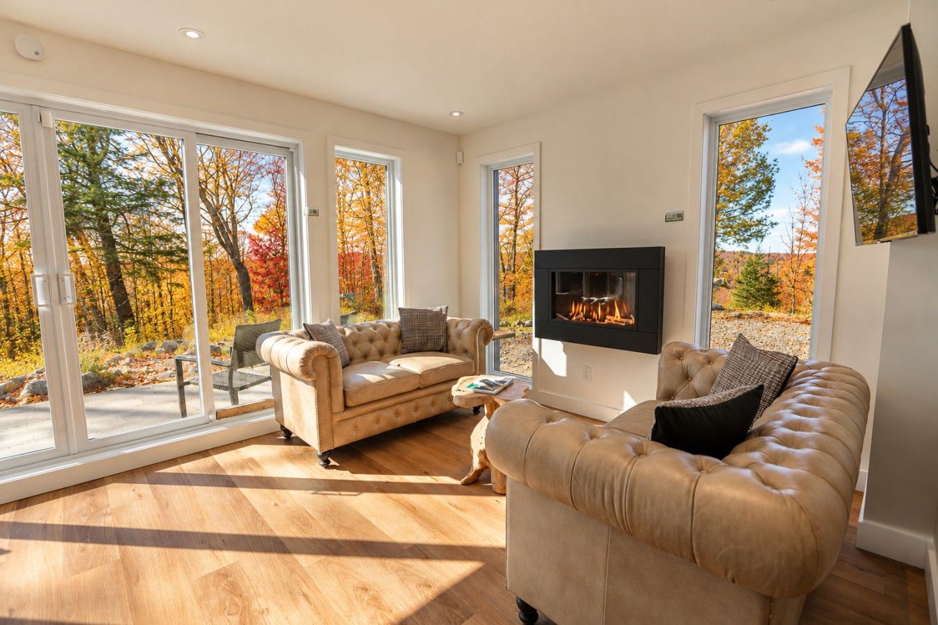 A spacious living room with a fireplace, large windows, and a view of autumn foliage.