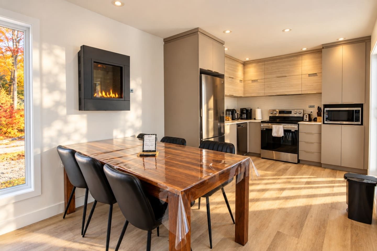 Una cocina moderna con comedor, chimenea y vistas al follaje otoñal.
