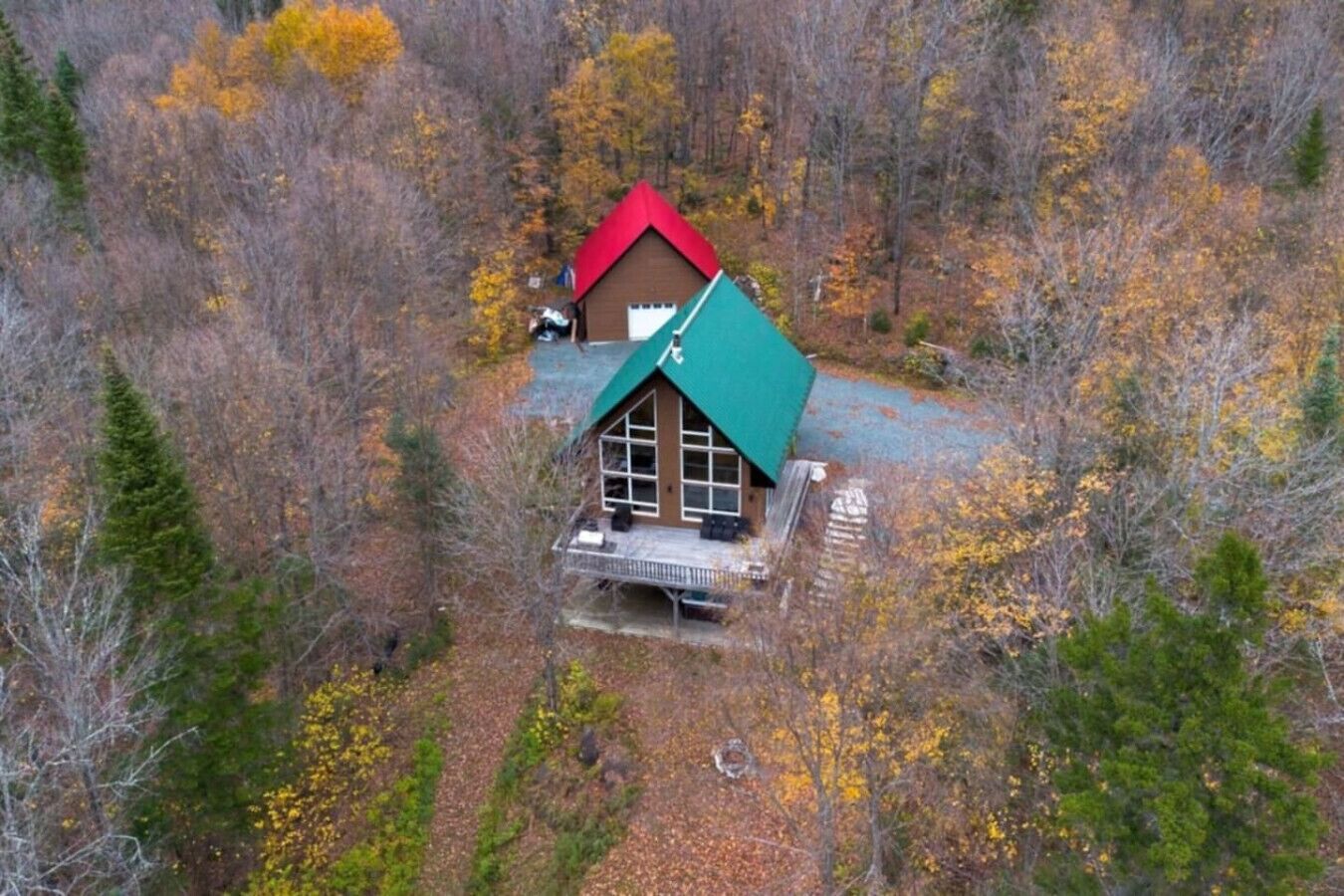 A cabin with a green roof and a red roof, surrounded by autumn foliage.