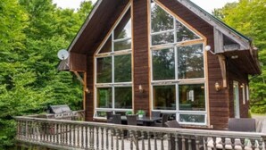 Una cabaña de madera con ventanas amplias, una terraza y mobiliario exterior.