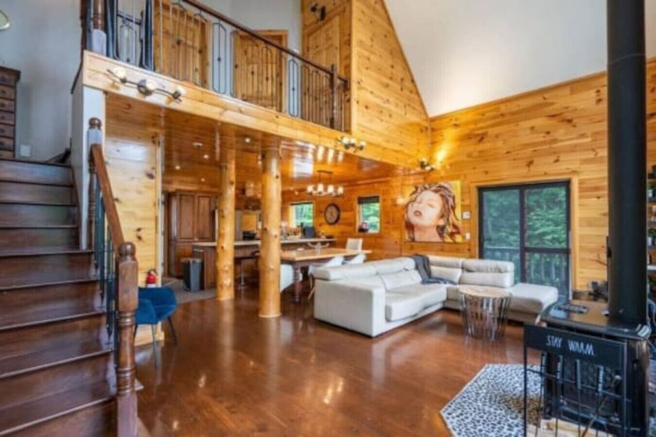 A spacious log cabin interior with a large living area, a dining area, and a staircase leading to a loft.