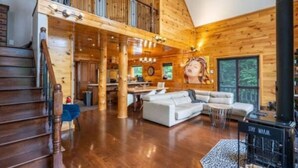 Un interior espacioso de cabaña de troncos con una amplia sala de estar, un comedor y una escalera que lleva a un altillo.