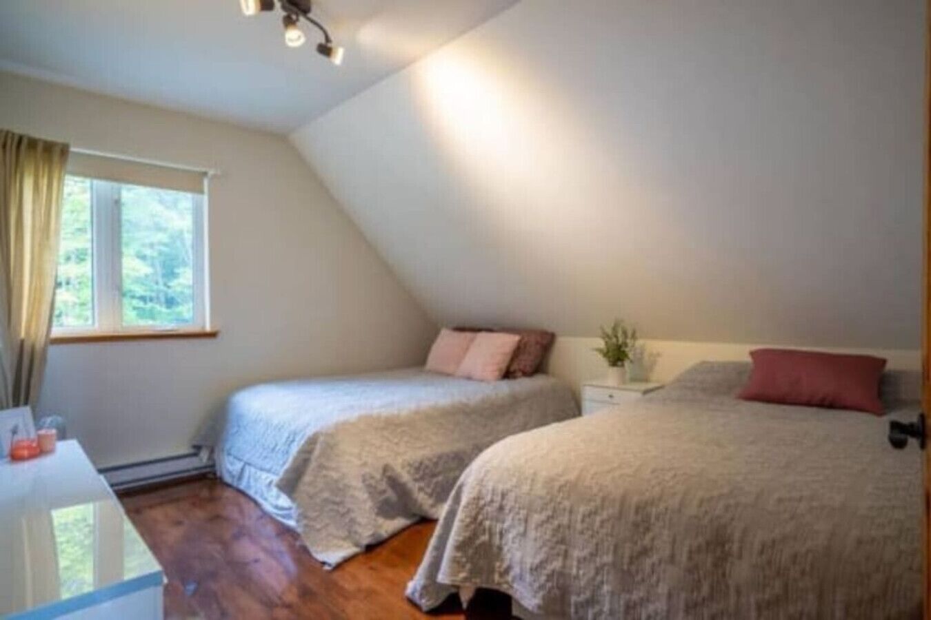 A bedroom with two beds, a bedside table, a window with curtains, and a ceiling light fixture.