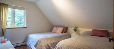 A bedroom with two beds, a bedside table, a window with curtains, and a ceiling light fixture.