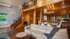 Un amplio espacio de estar con techo alto, paredes de madera, una escalera, un comedor y vistas al exterior.