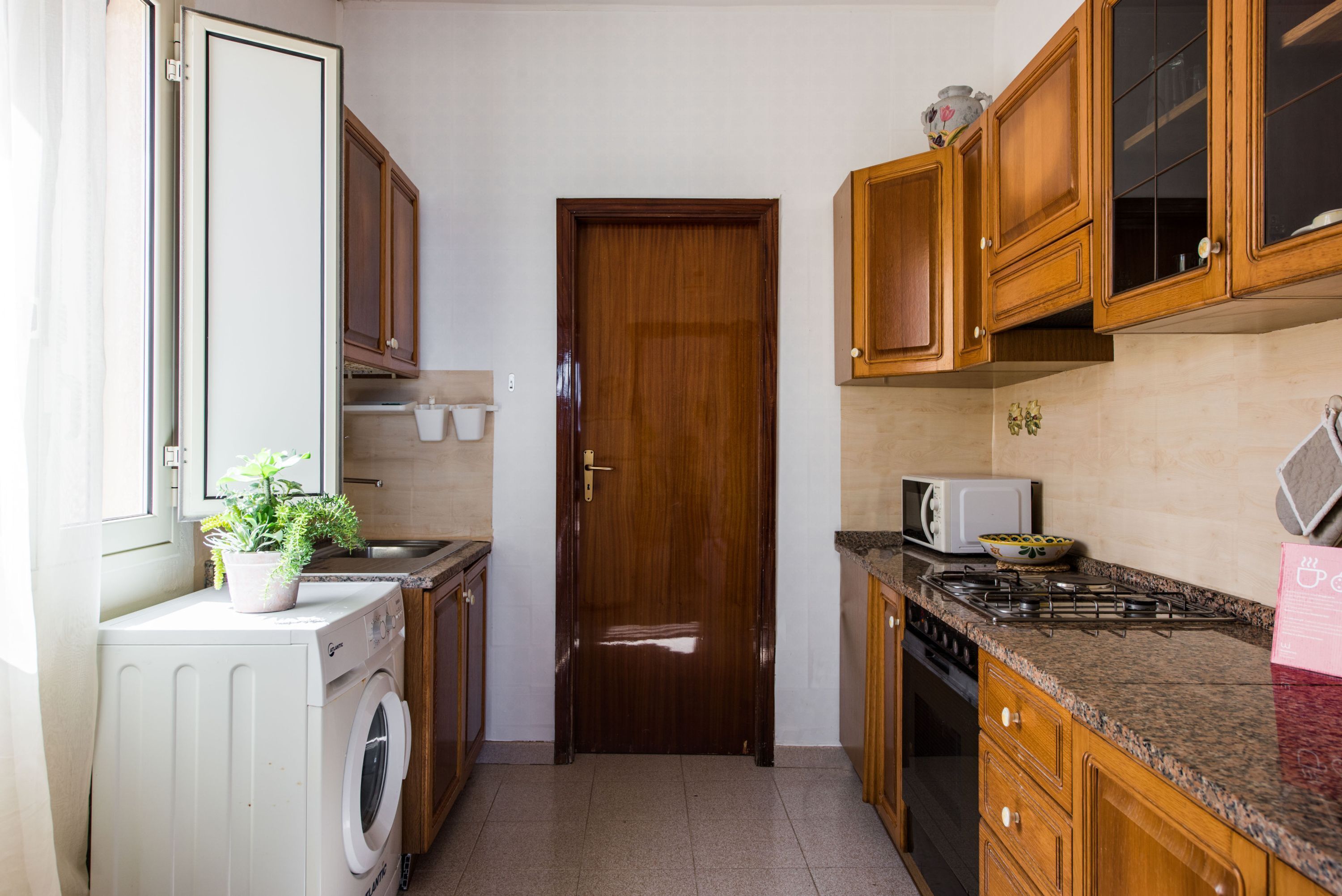 Een kleine keuken met houten kastjes, een magnetron, een fornuis en een wasmachine.