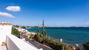 A coastal view with a clear blue sky, a road leading to a white building with a tiled roof, and a body of water in the background. - La Casa Dell Isola by Wonderful Italy (Syracuse)