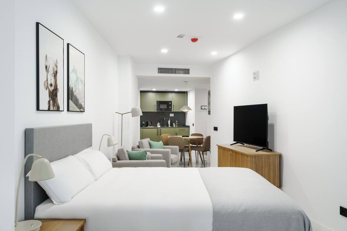 Una habitación de hotel moderna con una cama grande, televisor, escritorio y kitchenette.