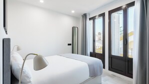 Una habitación de hotel moderna con una cama grande, una lámpara de noche, un espejo y vistas de la ciudad a través de amplias ventanas.