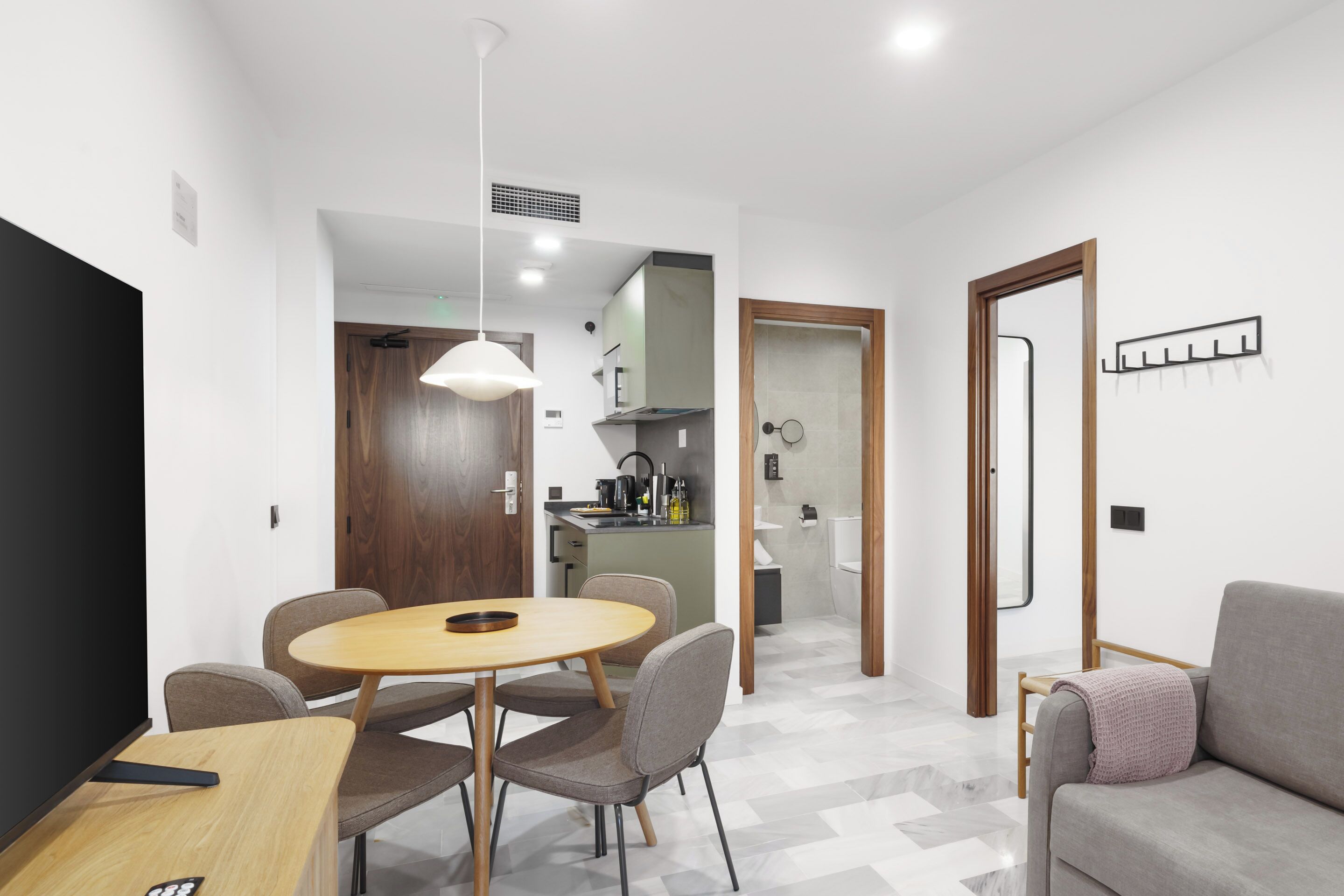 A modern living room with a round wooden dining table, grey sofas, and a grey couch.