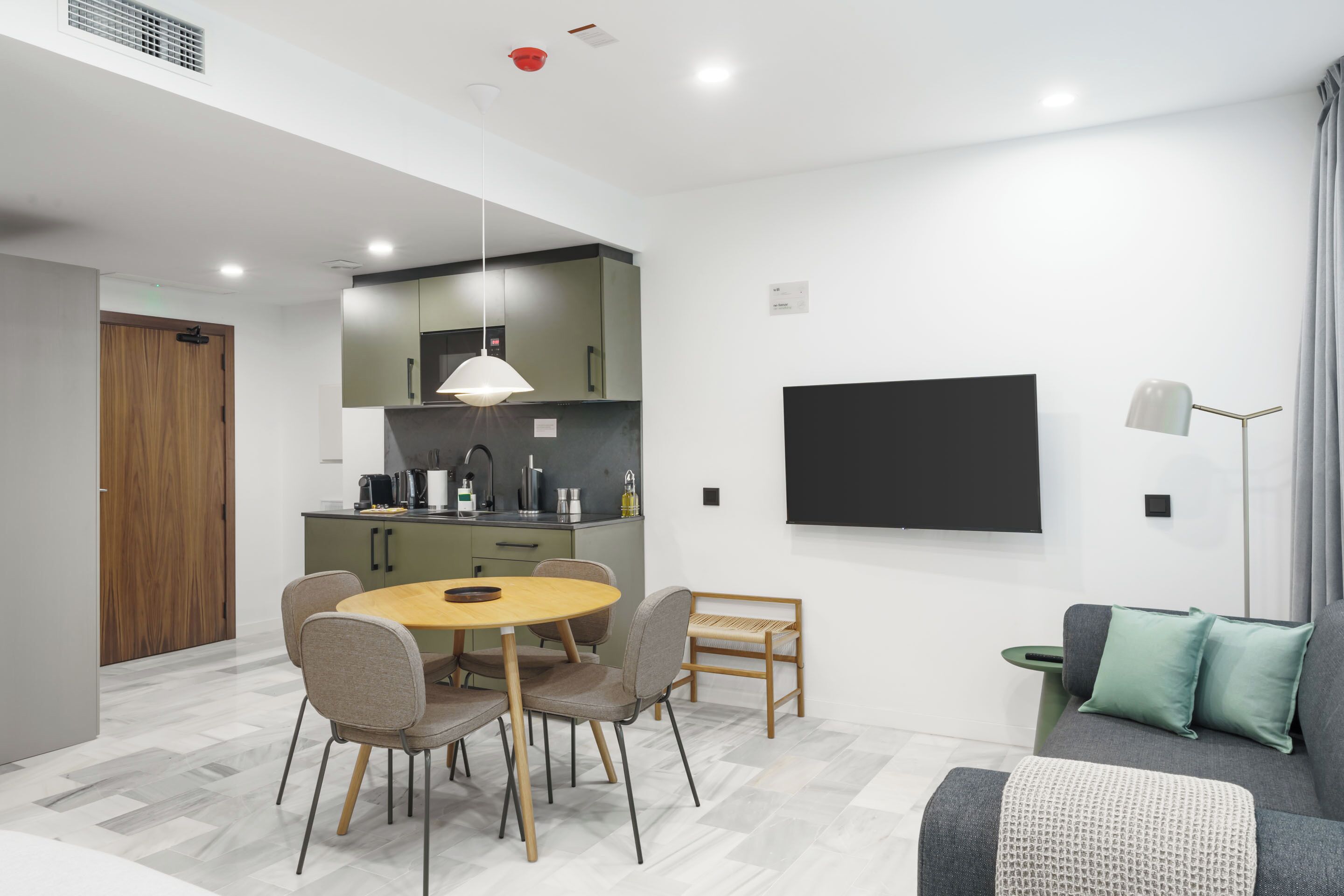 Uma sala de estar moderna com sofá, mesa de jantar com cadeiras, cozinha com pia e armários, e uma TV de tela plana na parede.