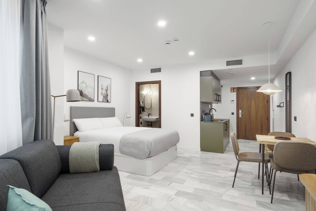 Una habitación de hotel moderna con cama, sofá, zona de comedor y kitchenette.